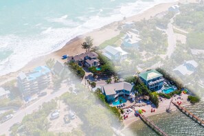 Vue aérienne d’une station balnéaire comprenant plusieurs bâtiments, une plage et un espace piscine.