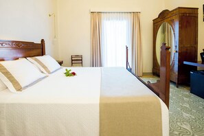 A neatly made bed with a white and beige bedspread, a wooden headboard, and a small rose on the bed. There is a wooden wardrobe with a mirror, a desk, and a chair in the room. - Bolet Casa Modernista (Castellvi de la Marca)