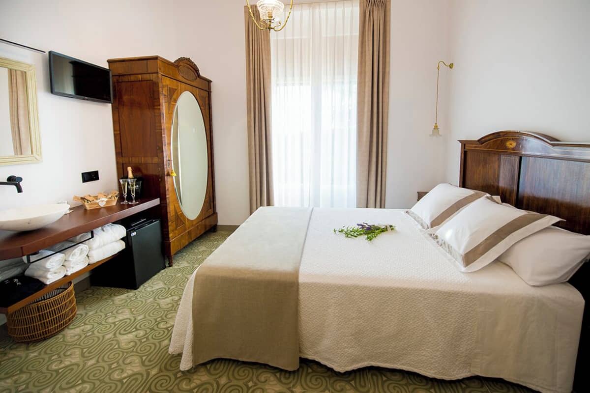 Una habitación de hotel con una cama, un tocador con espejo, un televisor, un armario de madera y una ventana con cortinas.
