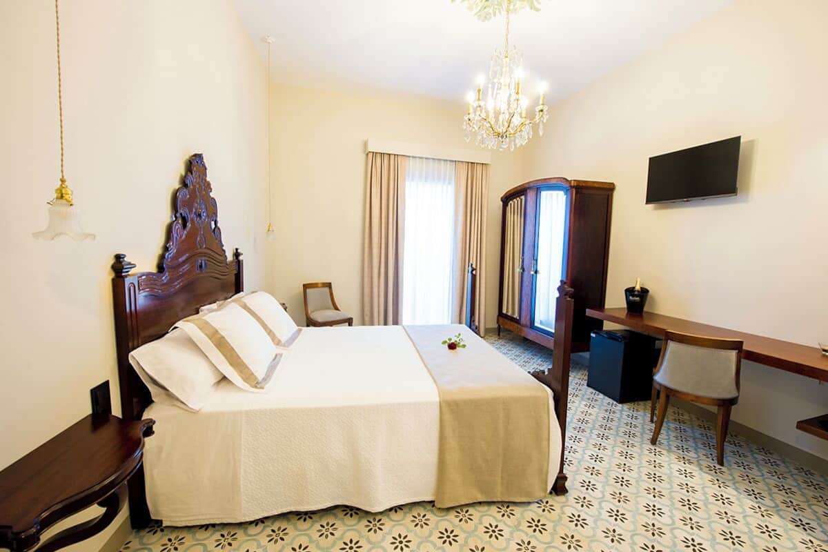 Una habitación de hotel con una cama grande, un escritorio, una silla, un televisor y una araña.
