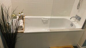 Ein modernes Badezimmer mit einer weißen Badewanne, einer Duschkabine aus Glas und einer hölzernen Sitzbank.
