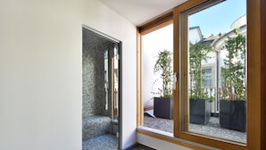 A modern bathroom with a glass shower enclosure, a built-in bench, and a large window offering a view of the outside. - HOTEL ROUSSEAU PLUS (Geneva)