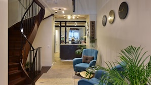 A modern lobby with a wooden staircase, a reception desk, and a blue armchair. - HOTEL ROUSSEAU PLUS (Geneva)