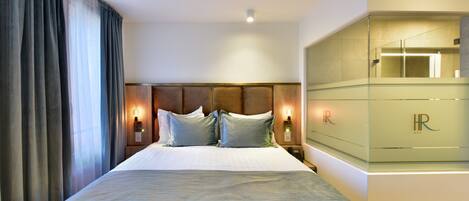 A hotel room with a large bed, a nightstand with a lamp, and a glass cabinet with a mirror.
