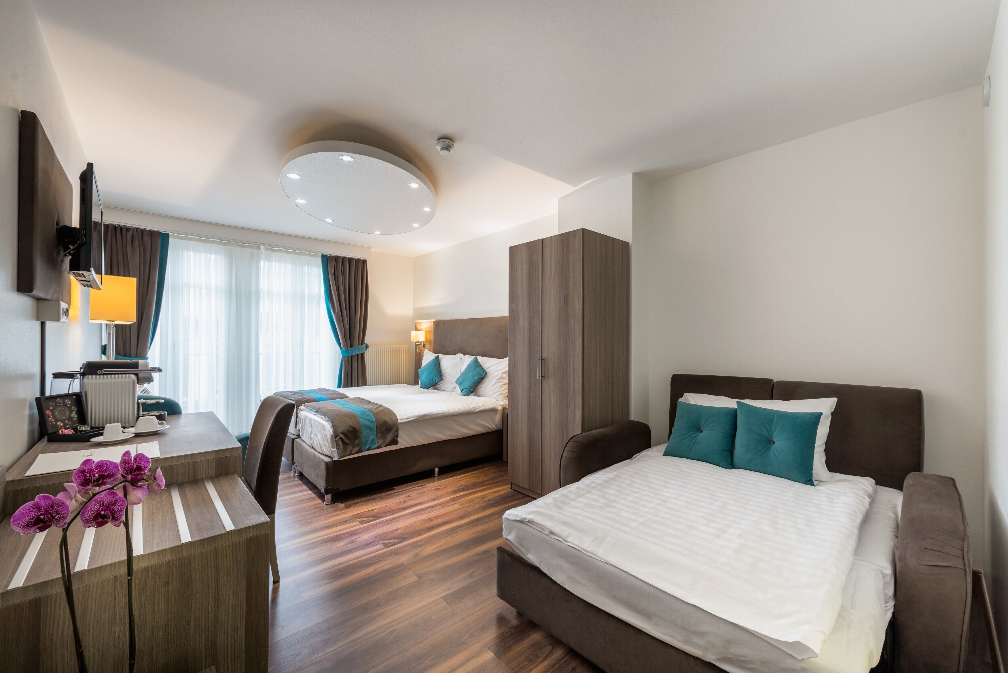 Una habitación de hotel moderna con una cama grande, otra más pequeña, un escritorio con una computadora y una zona de estar.