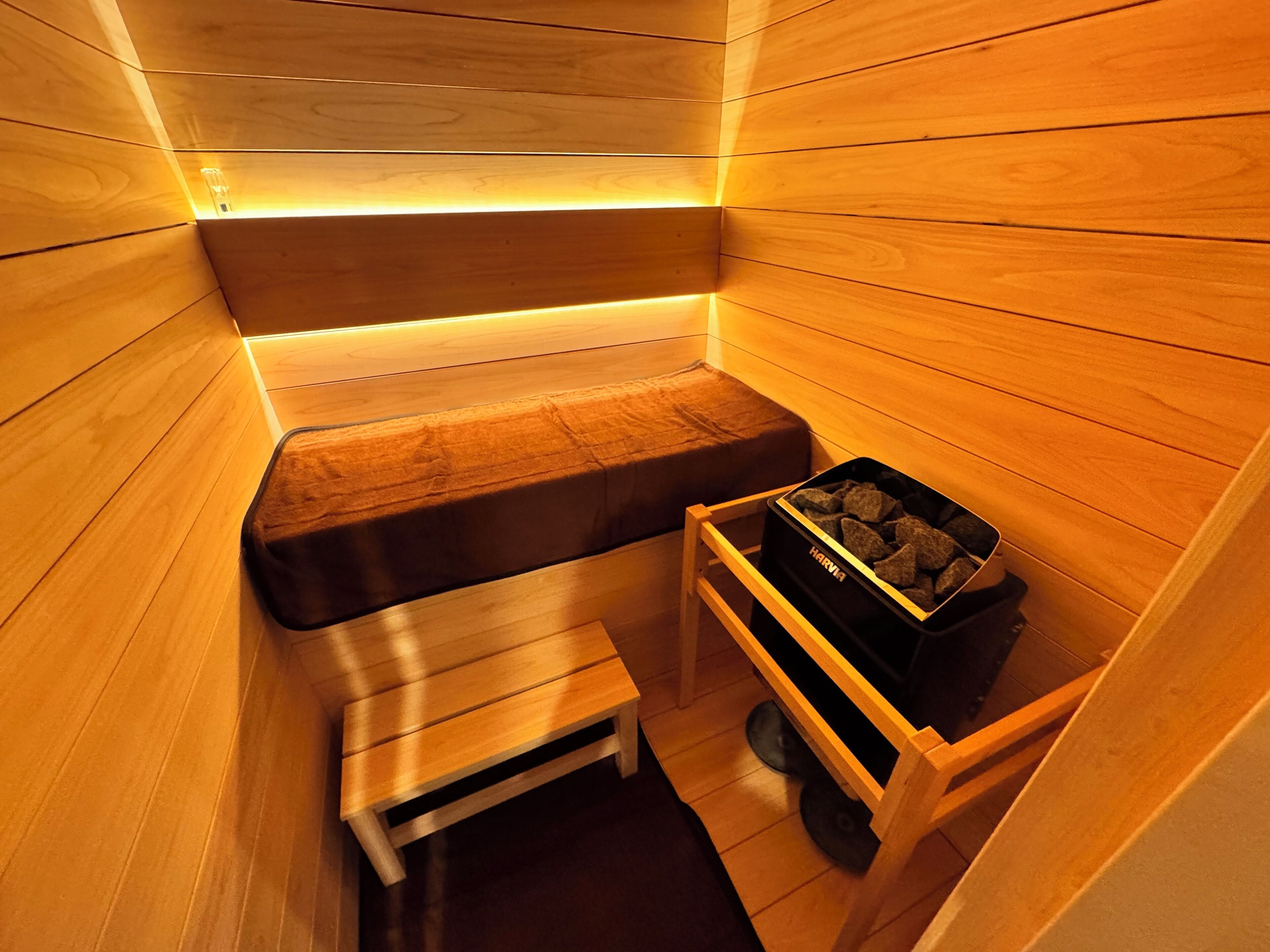 A sauna with wooden walls and benches, a small wooden table, and a storage bin labeled "HARVIA".