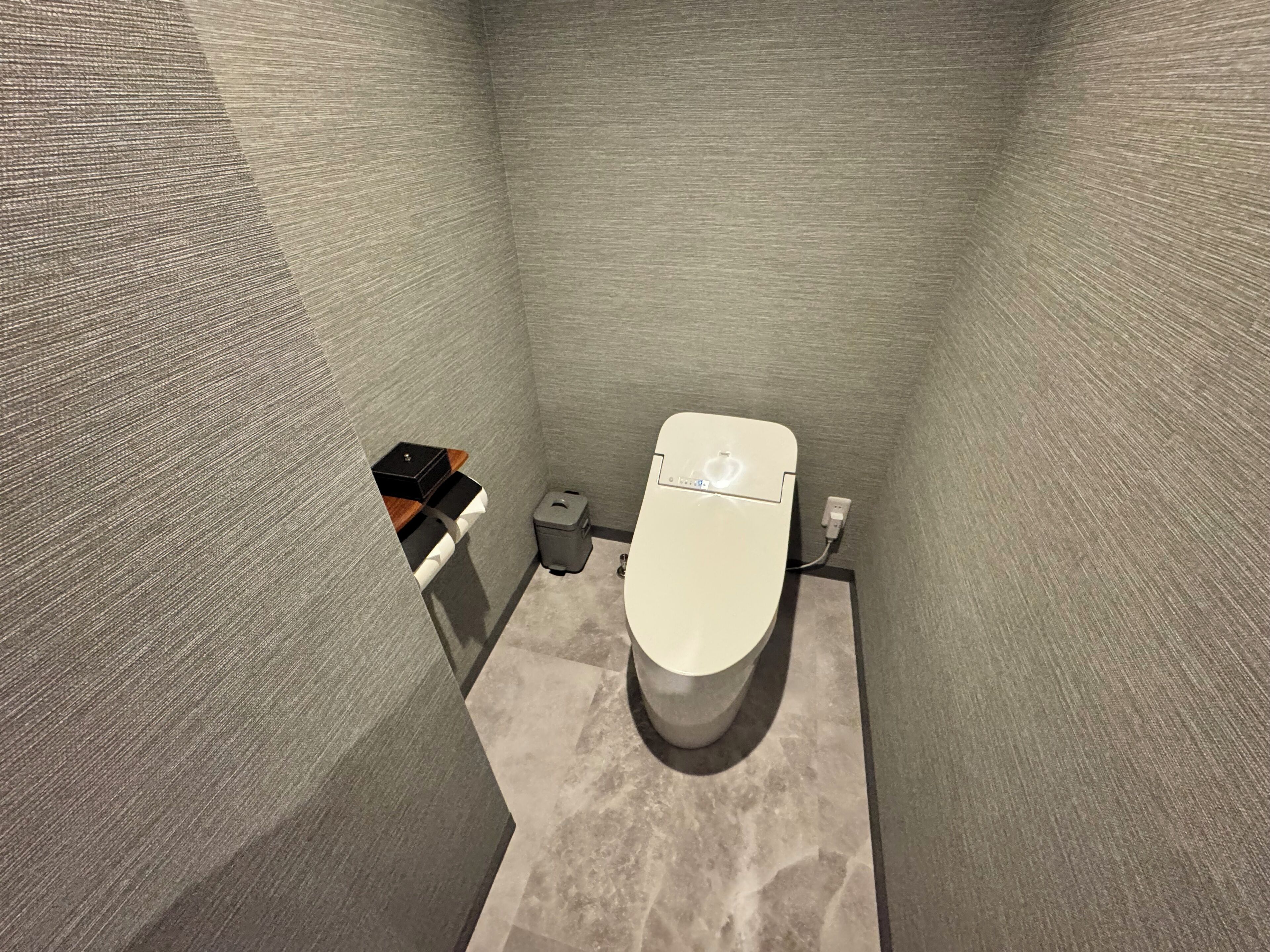 A small, narrow bathroom with a toilet, a trash bin, and a small storage unit.