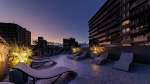 Een dakterras met lounge fauteuils en een versierd vloer, omgeven door gebouwen en een schemerige lucht.