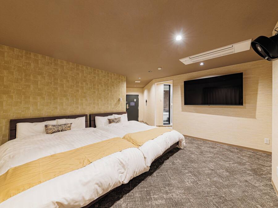 A hotel room with a large bed, a flat-screen TV mounted on the wall, and a ceiling-mounted air conditioning unit.