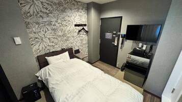A hotel room with a bed, a desk, a chair, a wardrobe, a mirror, a television, and a door with a lock.