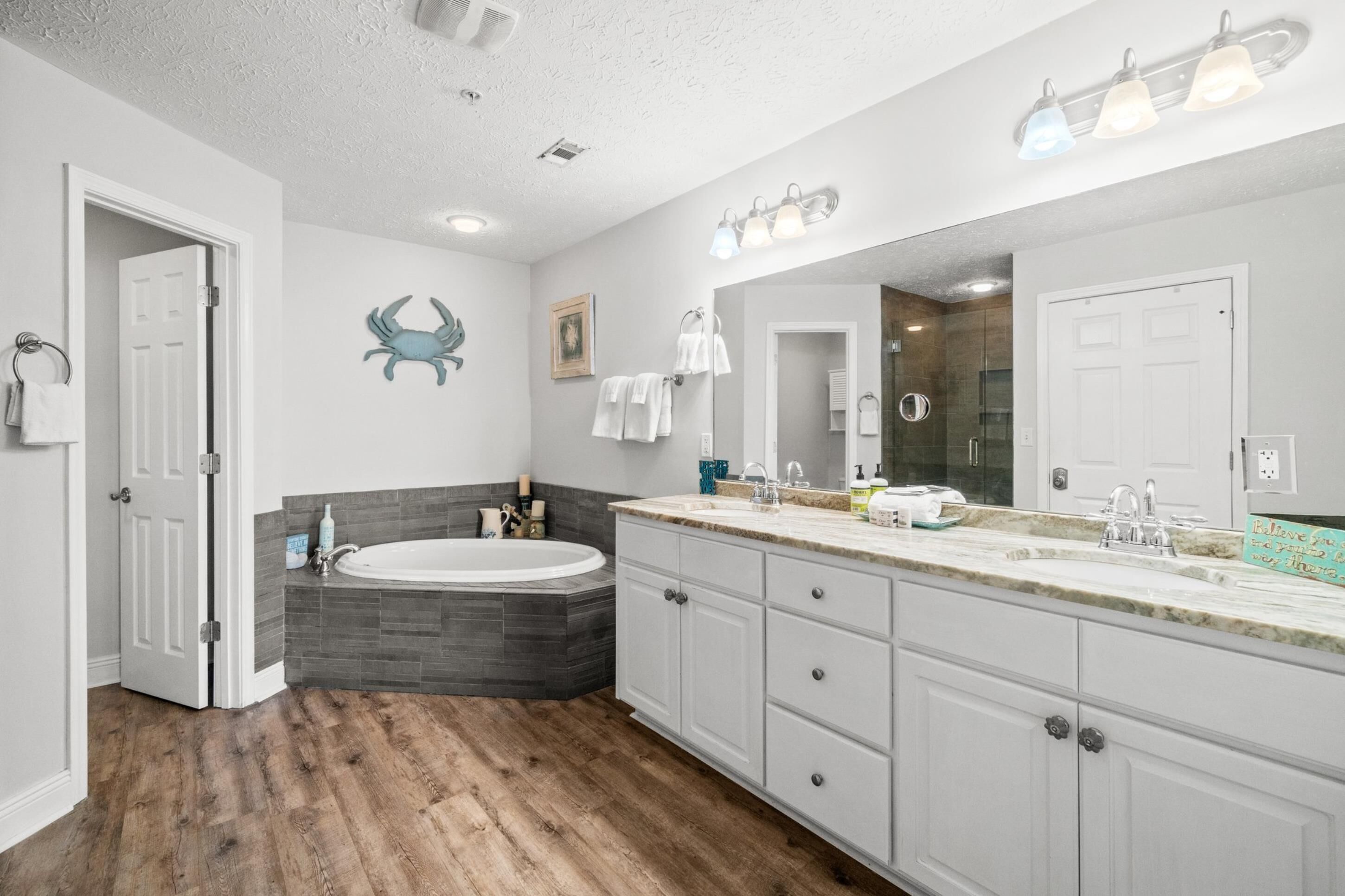A modern bathroom with a freestanding bathtub, a large vanity with a mirror, and a wooden floor.