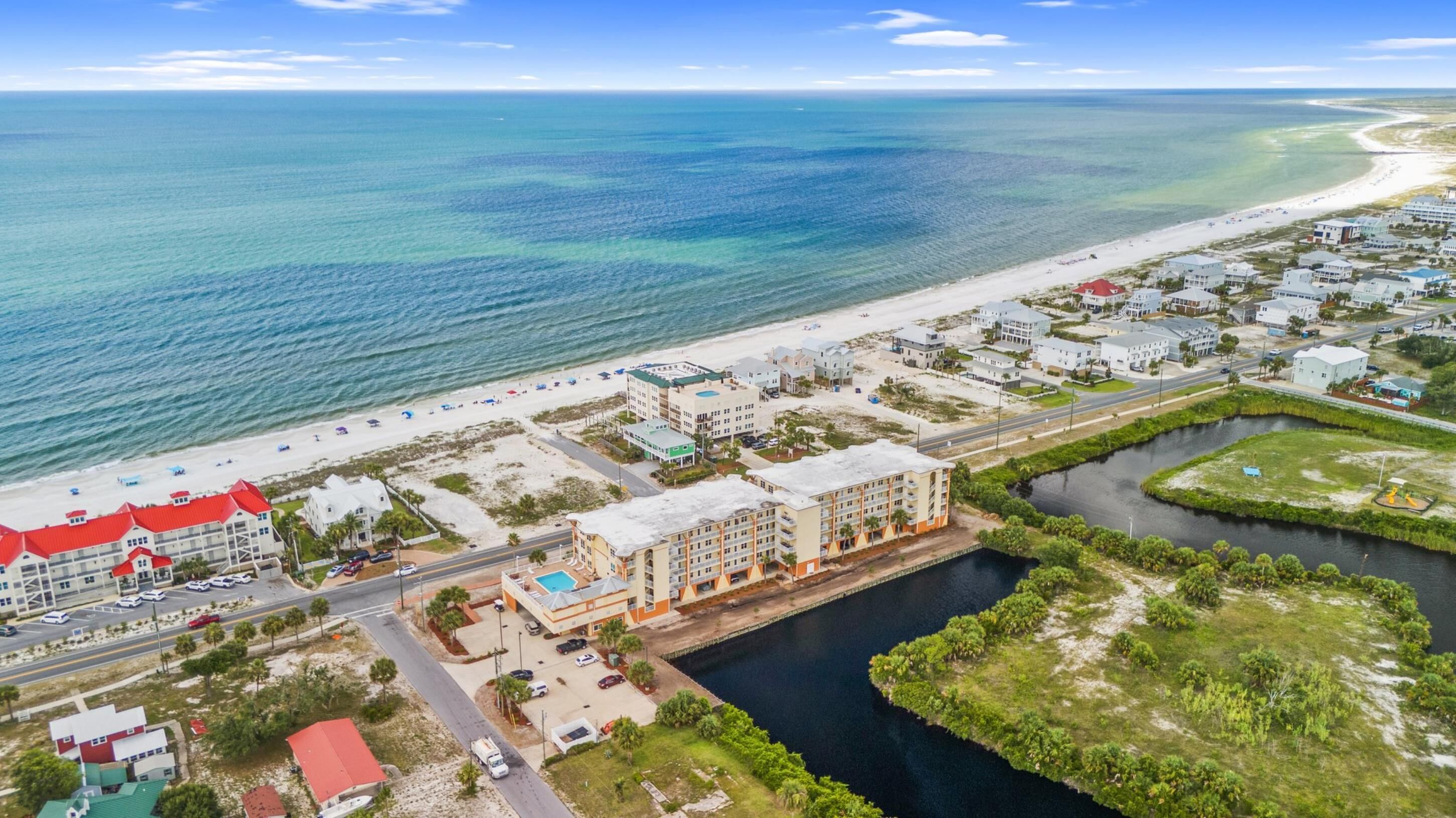 An aerial view of a coastal area with a beach, a marina, and several buildings including hotels.