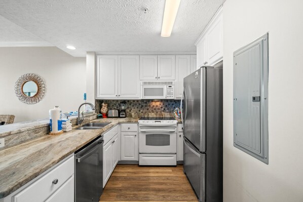 A modern kitchen with white cabinets, stainless steel appliances, a microwave, oven, and refrigerator.