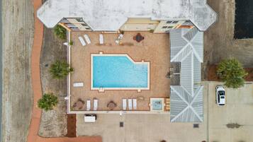 An aerial view of a property with a swimming pool, lounge chairs, and a parking area.
