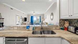 A kitchen with a marble countertop, stainless steel sink, and white cabinetry. There is a bag of flour, a toaster, and a decorative wreath on the wall. - Mexico Beach - Summerhouse by PHG (Port St. Joe)