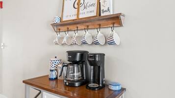 A kitchen counter with two coffee makers, a coffee pot, and a mug rack above.