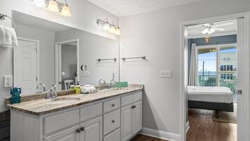 A bathroom with a large mirror, a sink with a marble countertop, and a vanity with drawers. There is a towel rack on the wall and a ceiling fan in the corner.