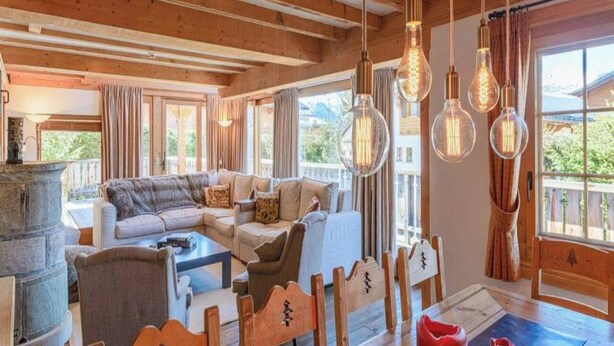 A cozy living room with a sofa set, wooden dining table, and hanging light fixtures. - Luxurious Alpine Retreat in Verbier Place Centrale with Panoramic Mountain Views (Val de Bagnes)