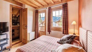 A bedroom with a bed, a television, a wardrobe, and a window with curtains. - Luxurious Alpine Retreat in Verbier Place Centrale with Panoramic Mountain Views (Val de Bagnes)