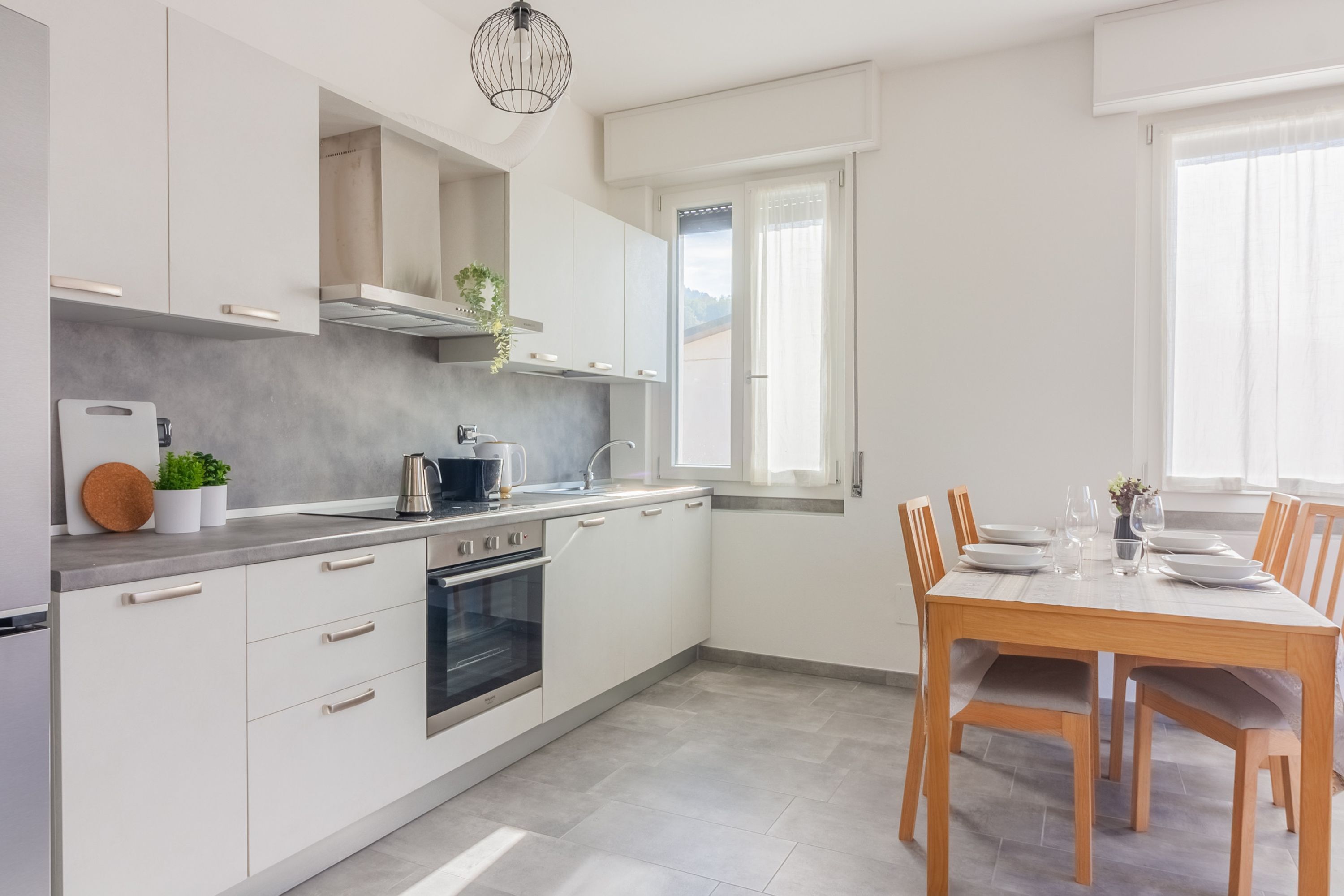 A modern kitchen with white cabinets, a built-in oven, and a dining area with a wooden table and chairs.