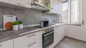 Una cucina moderna con mobili bianchi, forno in acciaio inossidabile, macchina del caffè e finestra con tende.