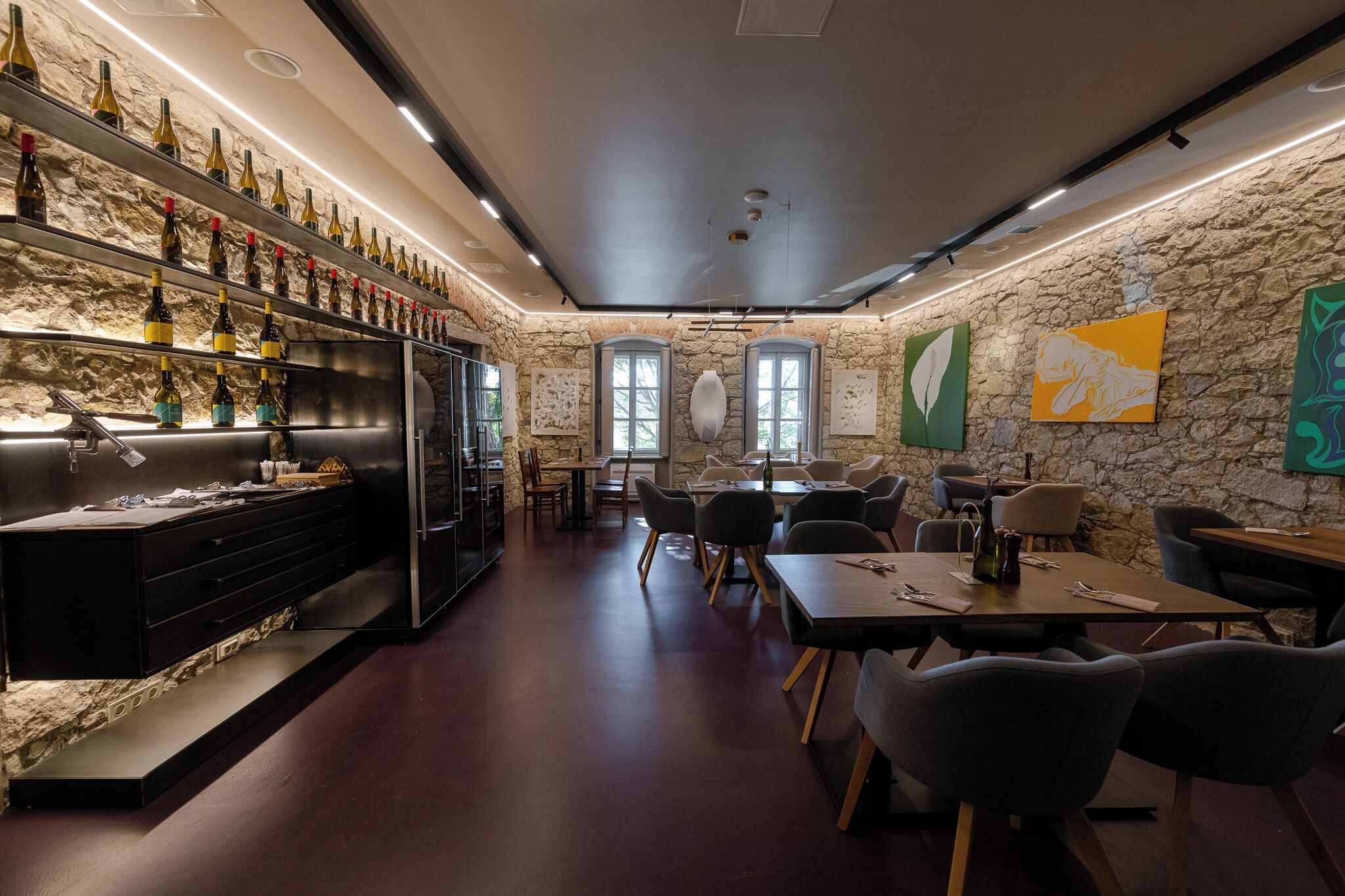 En restaurang med en vägg av sten, vinflaskor på hyllor och moderna möbler.