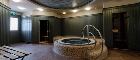 A spa area with a circular hot tub, a wooden bench, and a ceiling with a circular design.