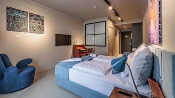 Una habitación de hotel moderna con una cama grande, un sillón azul, un escritorio y obras de arte en las paredes.
