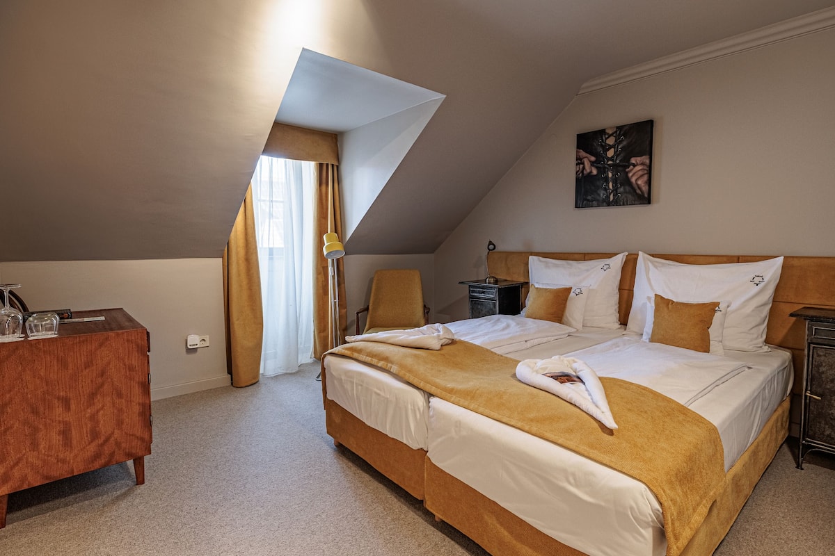 A hotel room with a large bed, a desk, a chair, and a painting on the wall.