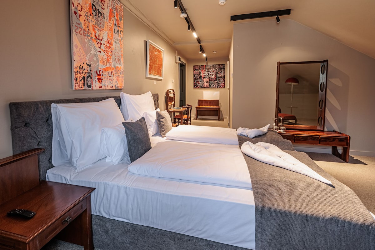 A modern hotel room with a large bed, a wooden nightstand, a desk, and a mirror.