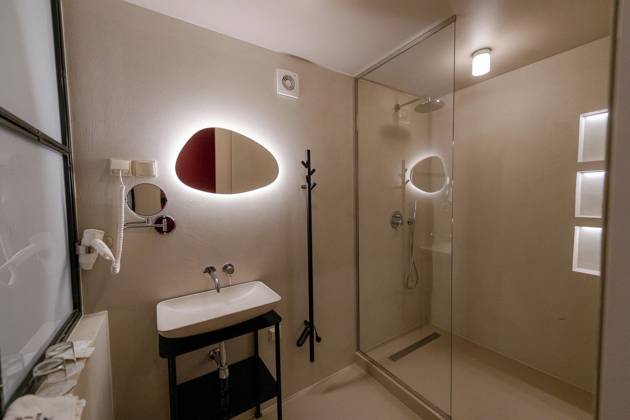 Een moderne badkamer met een douchecabine van glas, een wit wastafelmeubel en een spiegel met een rode accentkleur.