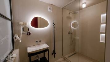 Een moderne badkamer met een douchecabine van glas, een wit wastafelmeubel en een spiegel met een rode accentkleur.