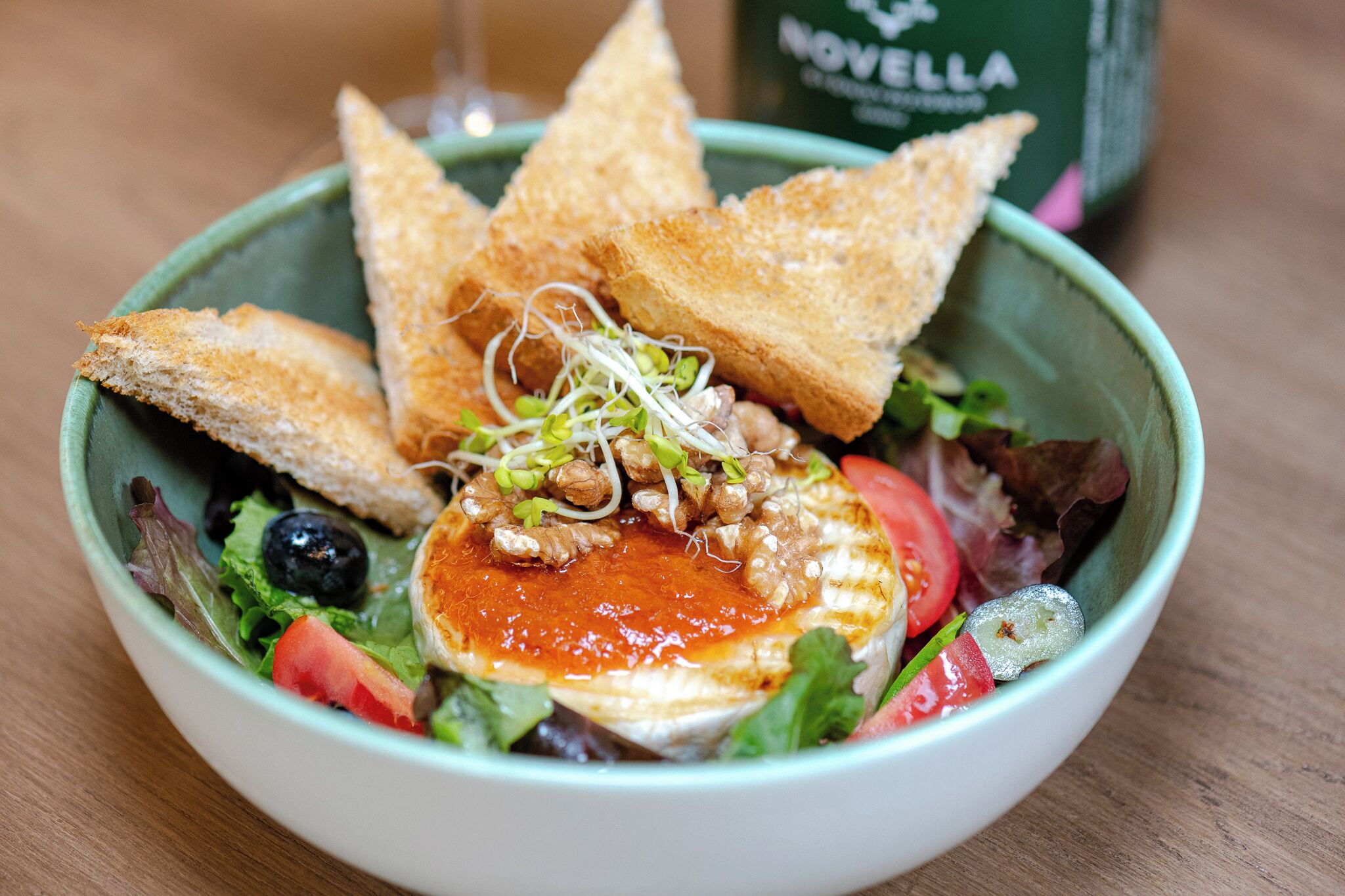 A bowl of salad with grilled chicken, sprouts, and a red sauce, accompanied by toasted bread slices.