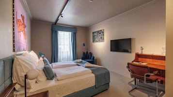 A modern hotel room with a bed, a desk, a chair, a lamp, and a TV.