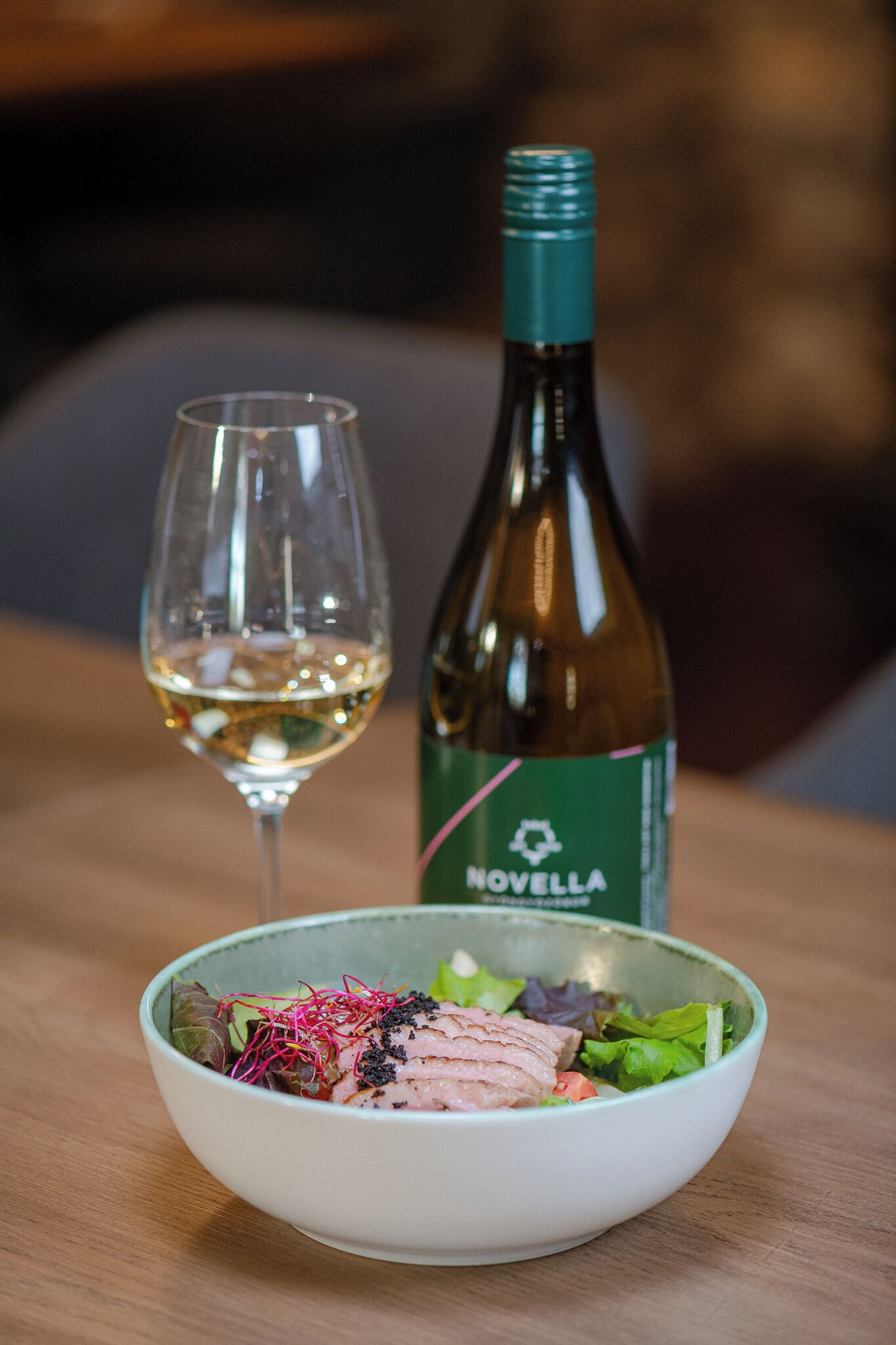 A bowl of food with a bottle of wine and a glass of wine on a table.