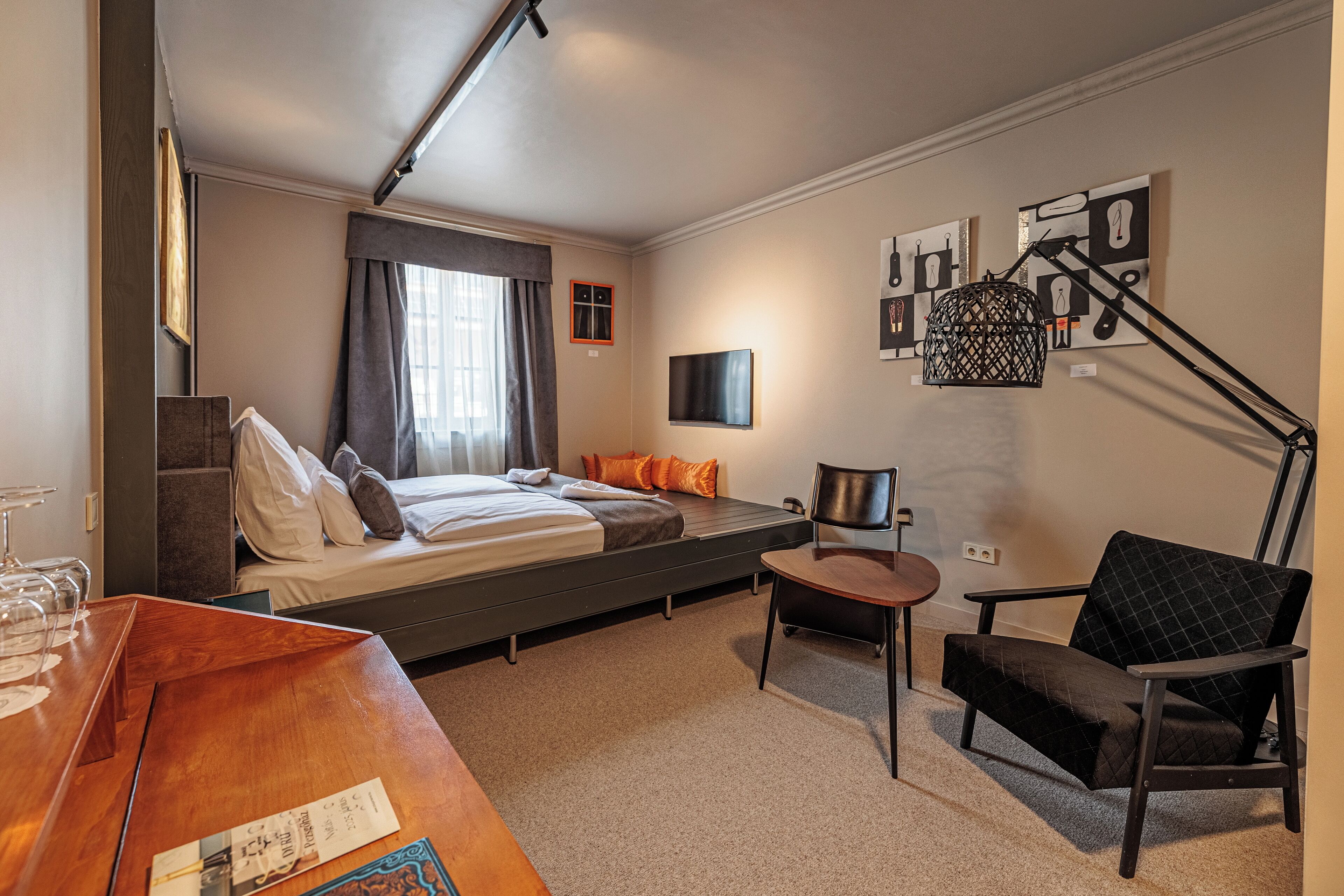 A modern hotel room with a bed, a desk, a chair, and artwork on the walls.