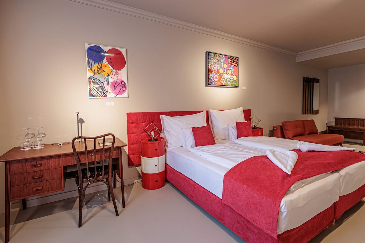 A hotel room with a large bed, a desk with a chair, and two paintings on the walls.