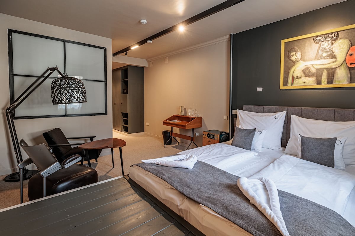 A modern hotel room with a large bed, a desk, a chair, and a painting on the wall.