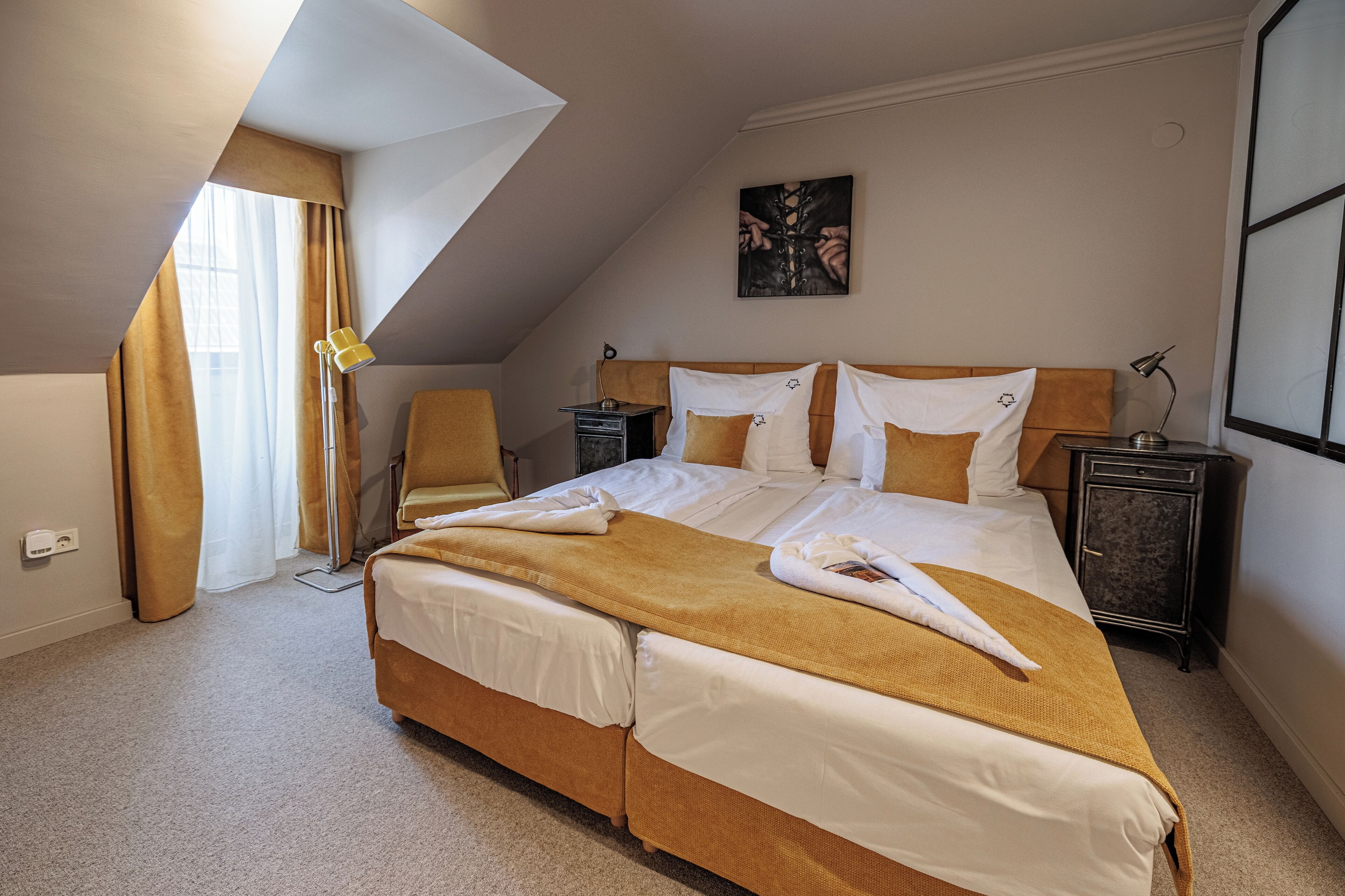 Quarto de hotel com uma cama grande, mesa de cabeceira, uma cadeira e um quadro na parede.