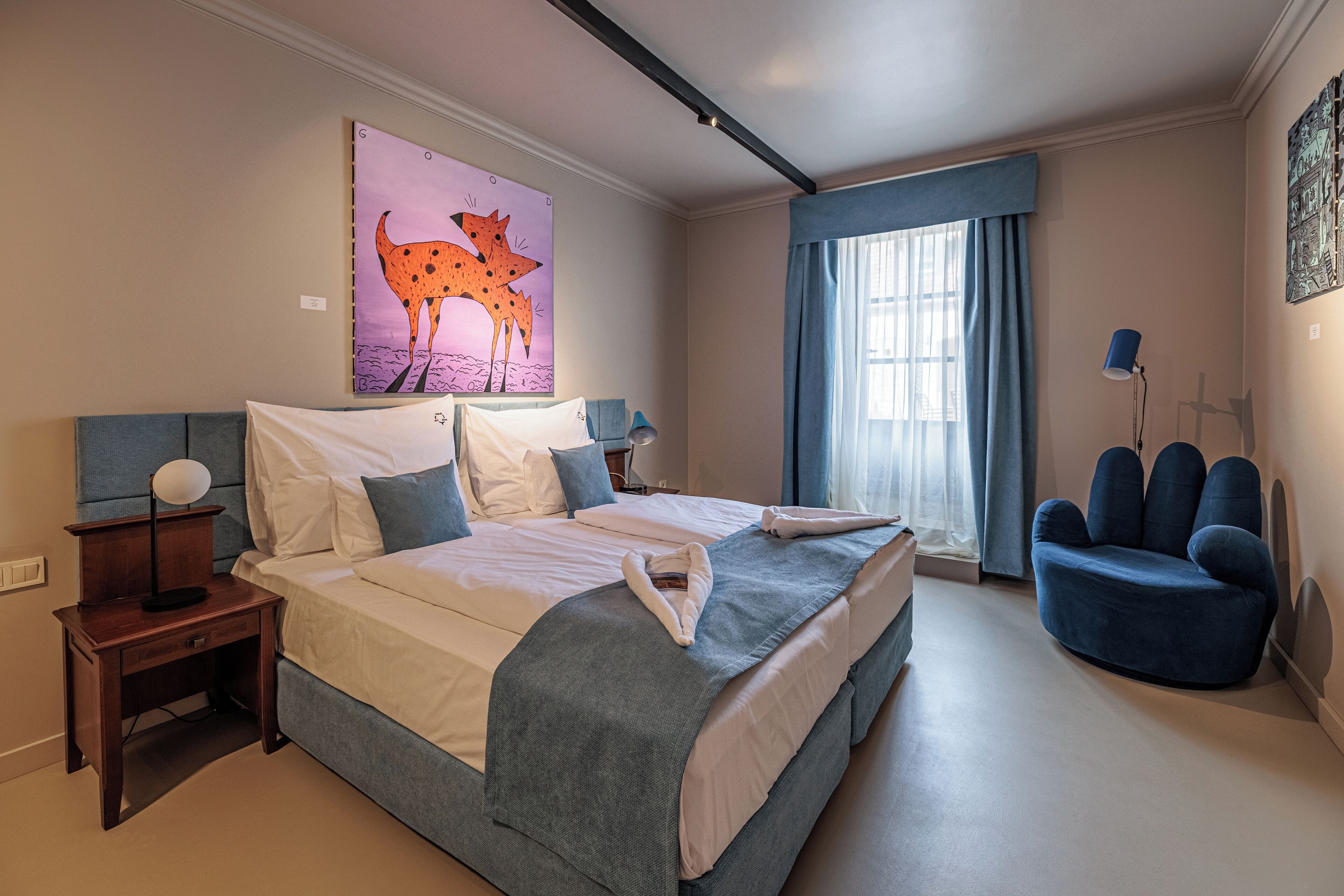 Una camera da letto con un letto grande, un comodino, una sedia, un quadro e una finestra con tende.