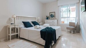 A bedroom with a bed, bedside tables, a chair, a window, and a painting on the wall. - Malta by BH Marbella (Marbella)