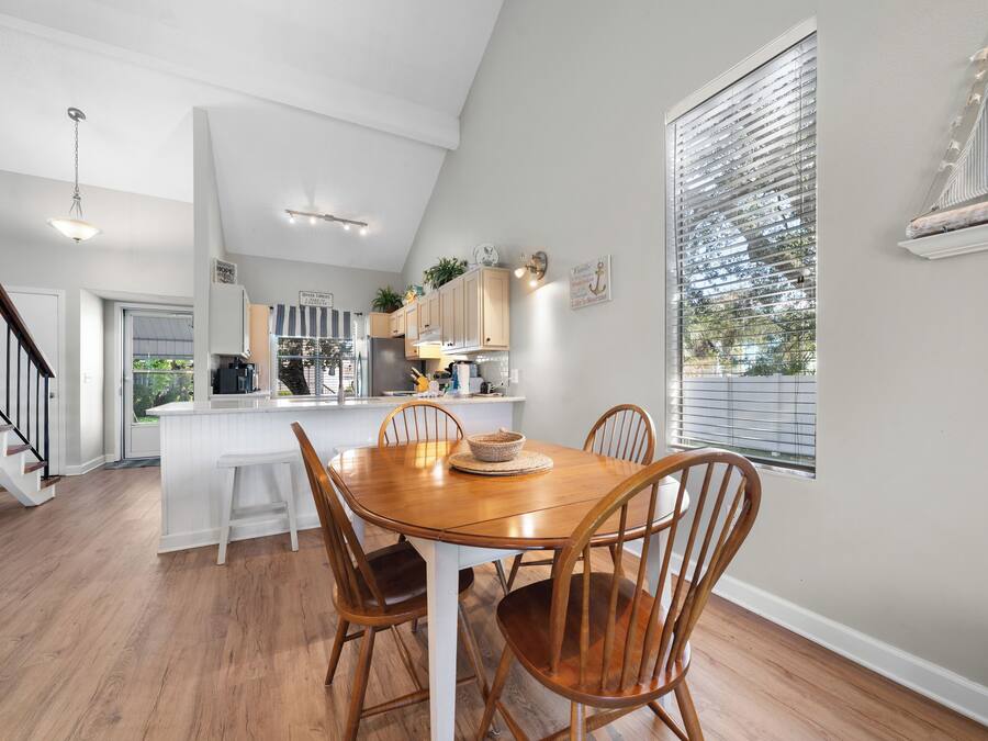 A modern kitchen with white cabinetry, a wooden dining table, and a staircase leading to another level.