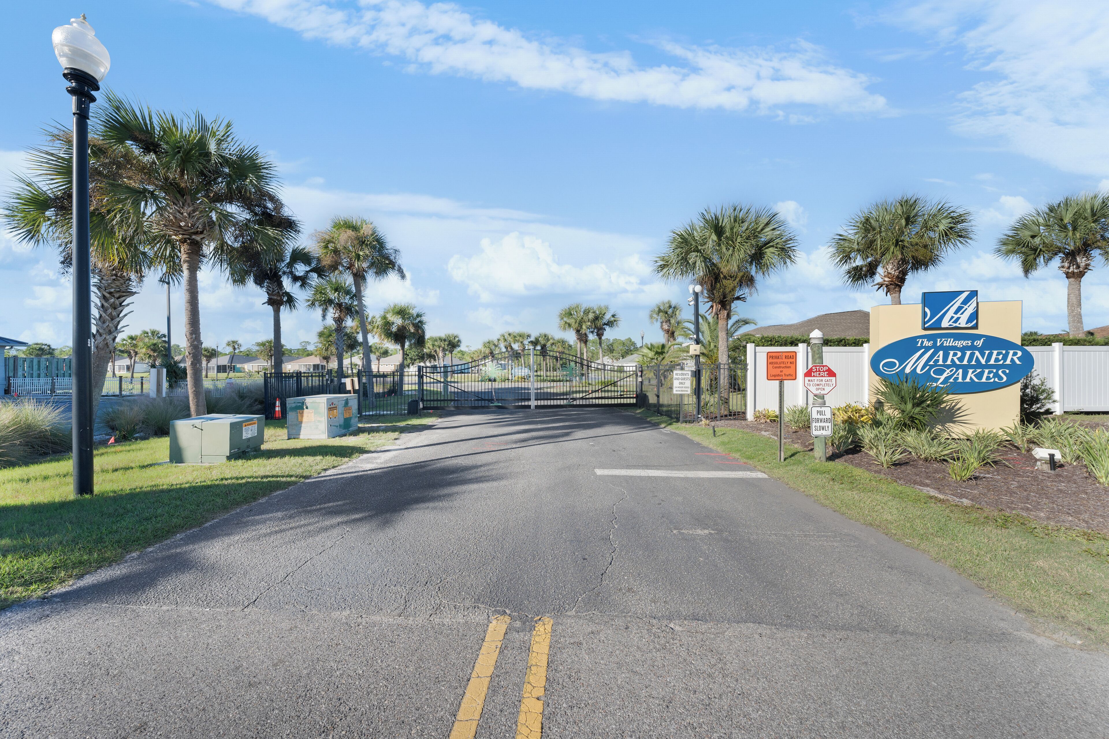 Een omheind toegangspunt naar The Villages of Mariner Lakes, met palmbomen en een heldere lucht.