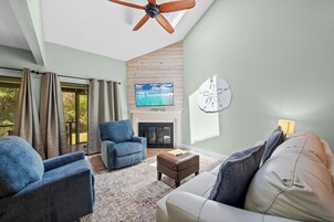 A living room with a fireplace, a ceiling fan, and a television displaying 'hosteva'.