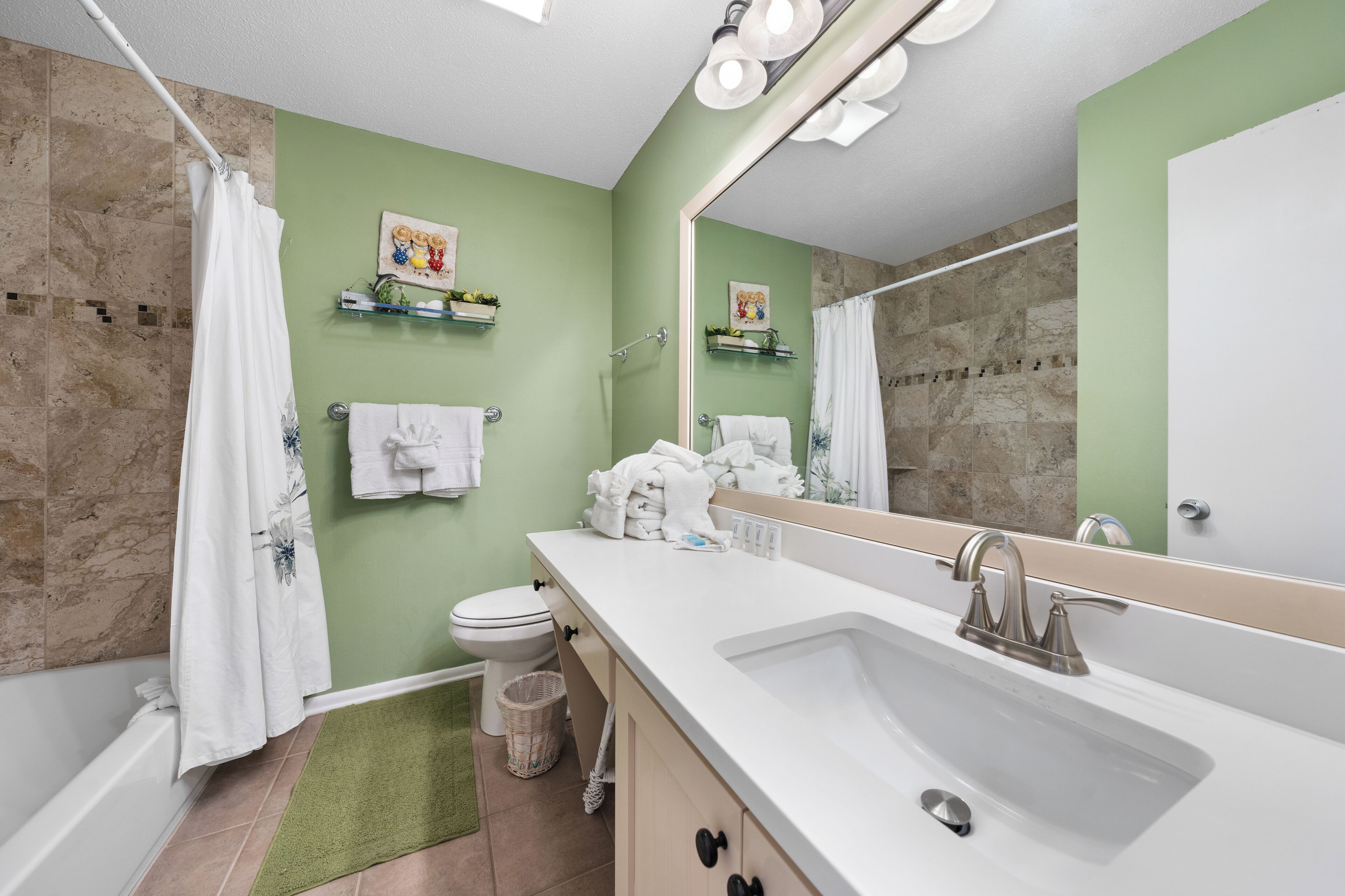 Un baño con bañera, inodoro, lavabo y un espejo grande.