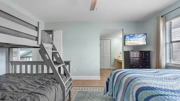 Une chambre avec un lit superposé, un bureau, une commode, une télévision et une salle de bain visible à travers une porte ouverte.