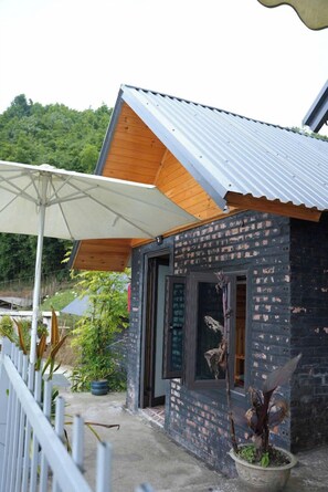 A small brick building with a wooden roof and a white umbrella. - Mama Lili's Homestay (Ta Van)