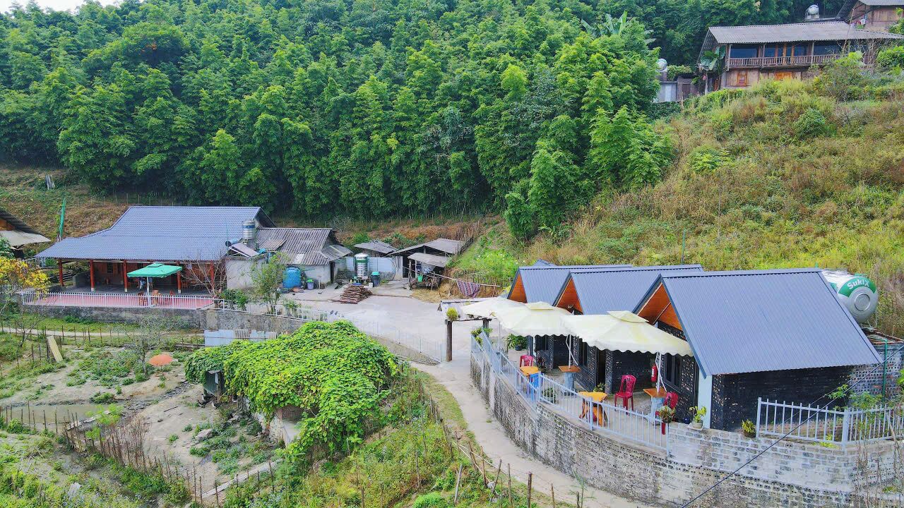 A rural guesthouse with multiple rooms, a small garden, and a path leading to a larger building.