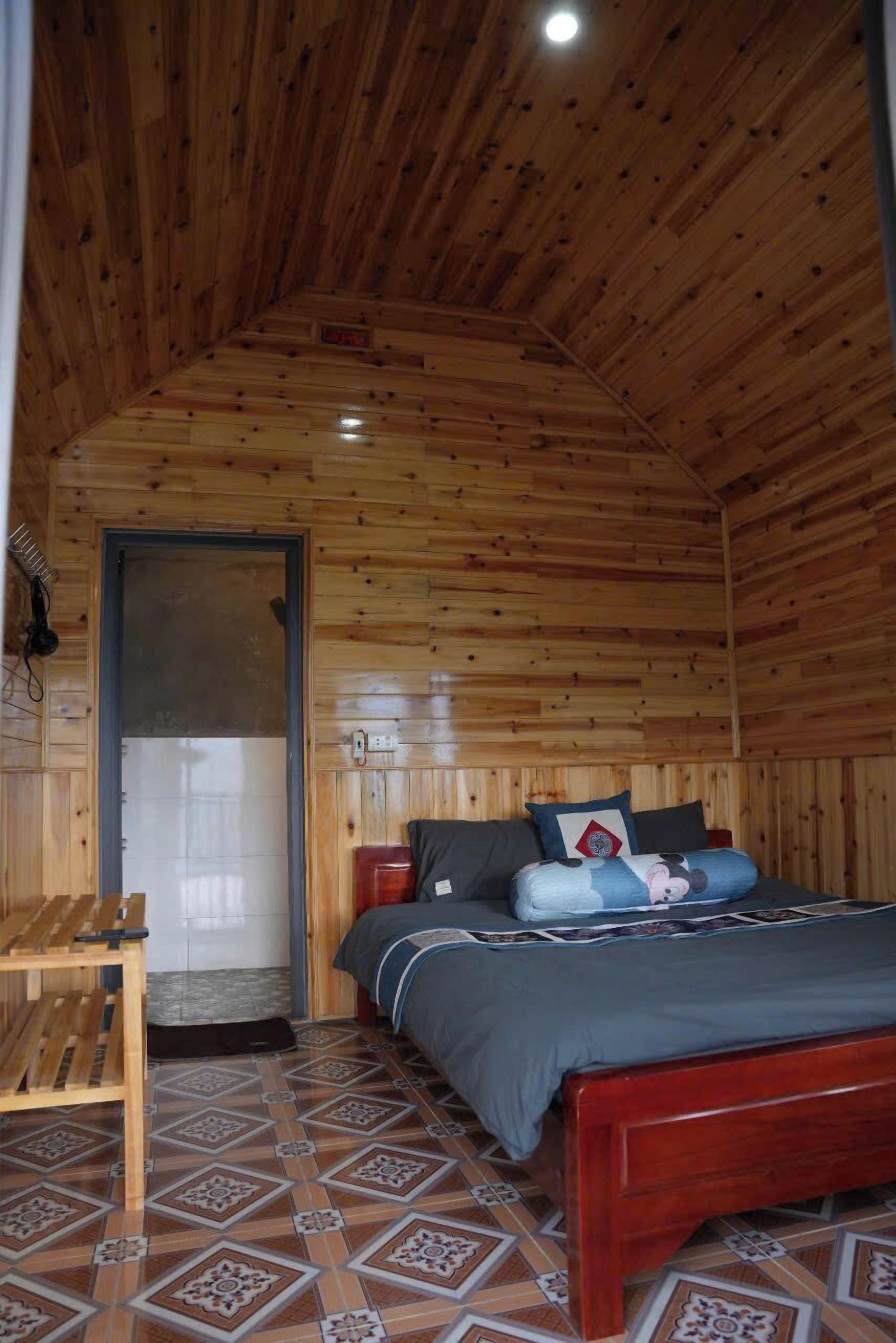Um quarto com painéis de madeira, uma cama, um banco de madeira e um chão estampado.