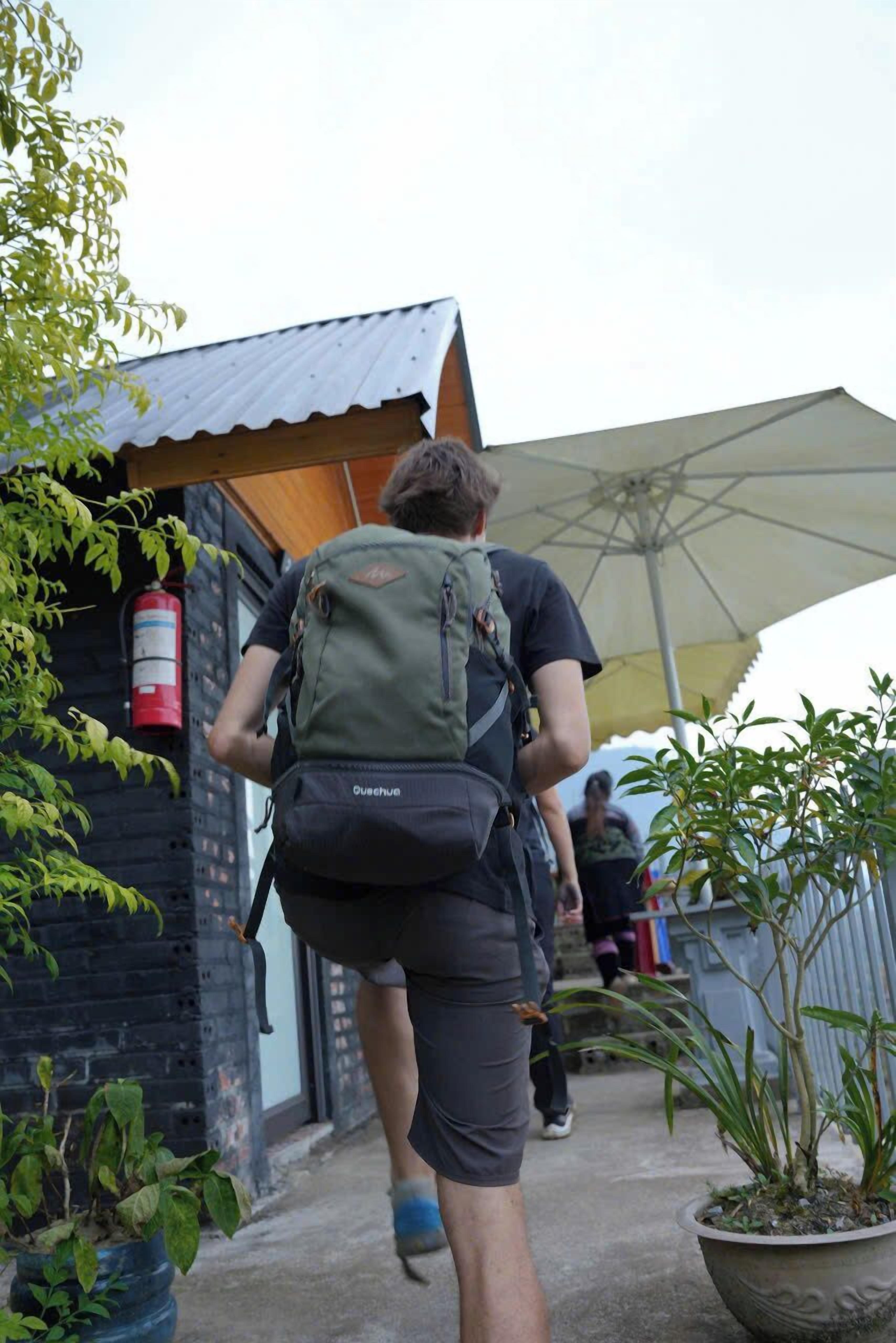 A person walking towards a building with a green backpack.